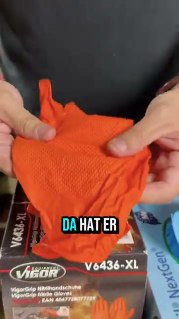 Hände dehnen einen orangefarbenen Vigor-VigorGrip-Handschuh mit sichtbarer Noppenstruktur; darunter die Verpackung „VIGOR V6436-XL VigorGrip Nitrilhandschuhe