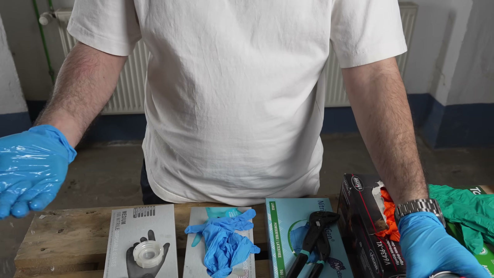 Der Tester mit blauen Nitrilhandschuhen am Testplatz; auf der Palette die Produktverpackungen (Action, Meditrade NextGen, Vigor V6436-XL, Ansell) und eine Zange für den Griptest.