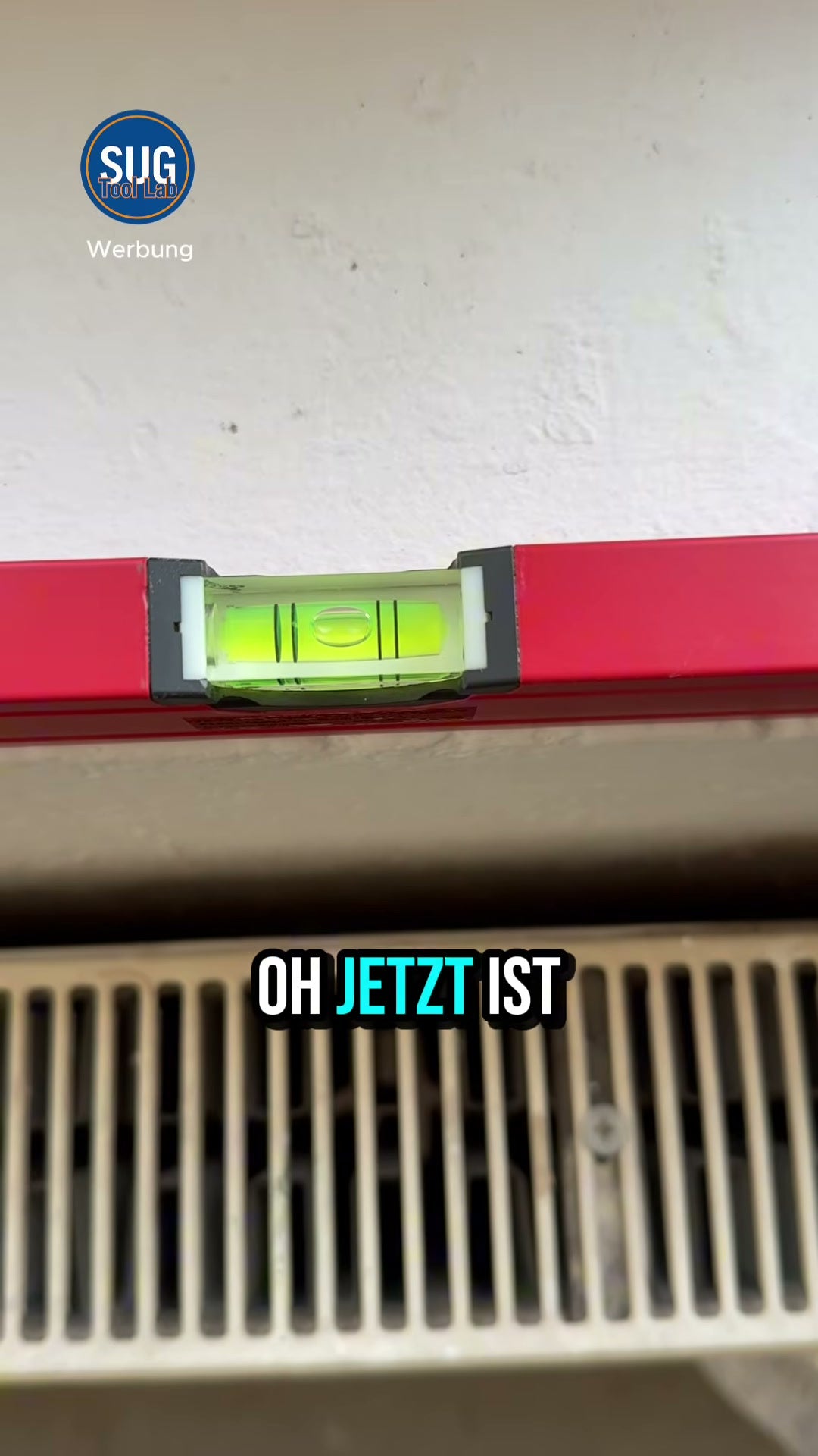 Nahaufnahme der Libelle einer roten Wasserwaage an einer Wand über einem Heizkörper während des 180-Grad-Umschlagtests; die Blase steht zwischen den beiden Markierungen.