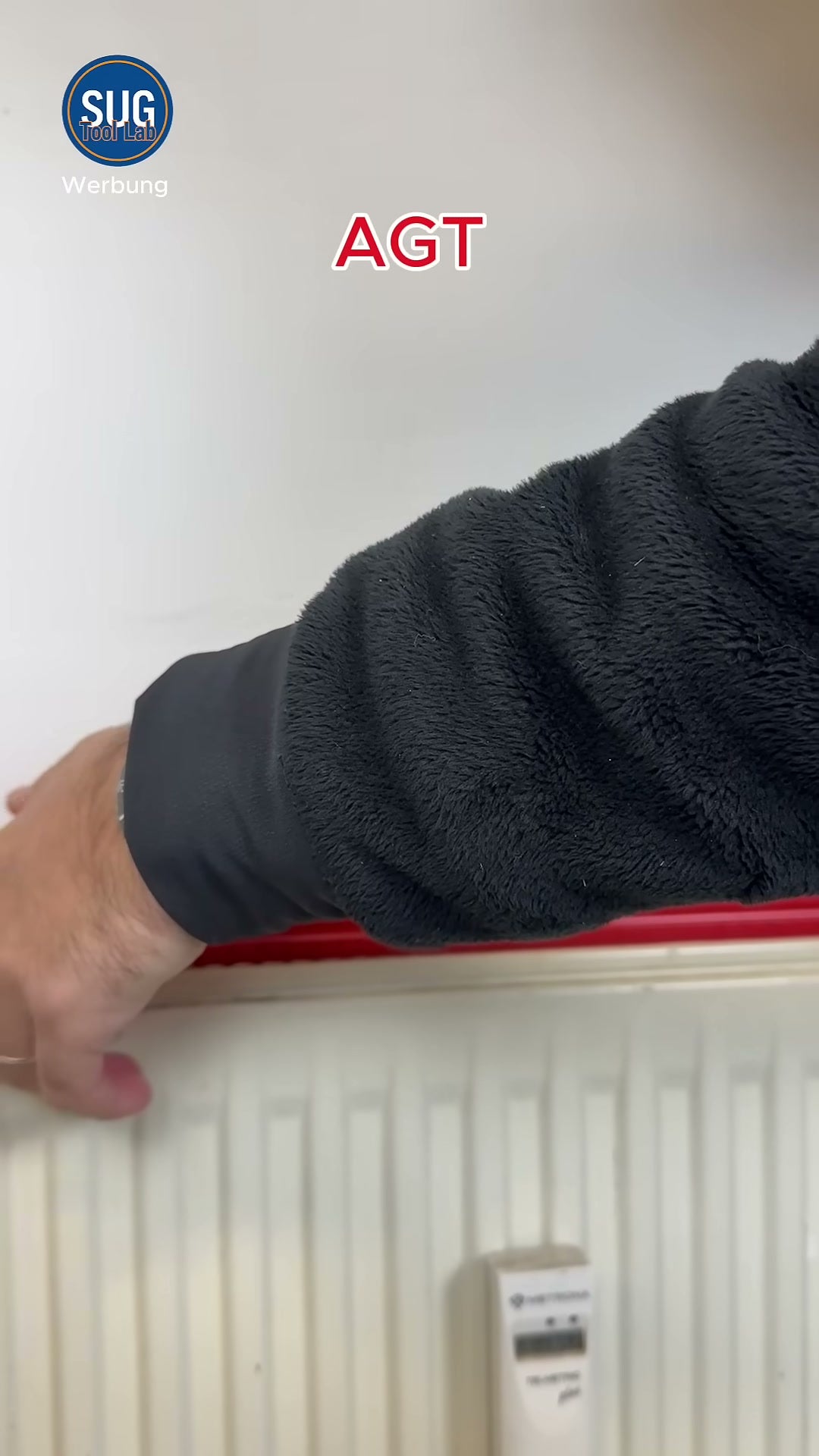 Der Tester belastet die rote AGT-Wasserwaage mit dem Unterarm auf einem Heizkörper; im Video als „AGT“ beschriftet.