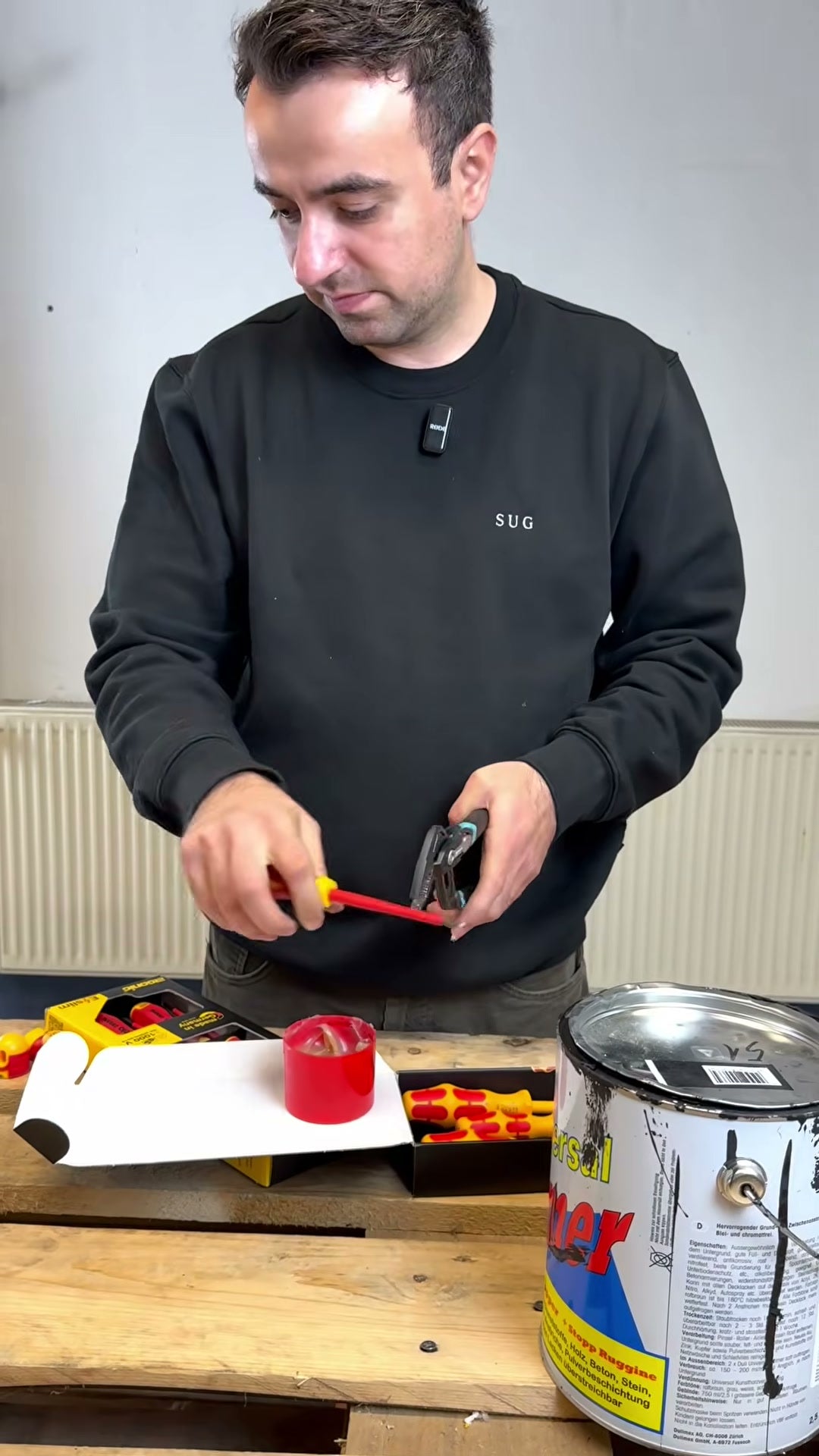 Der Tester fettet an der Werkbank einen Schraubendrehergriff ein, daneben stehen ein geöffneter Fettbehälter und ein Farbeimer