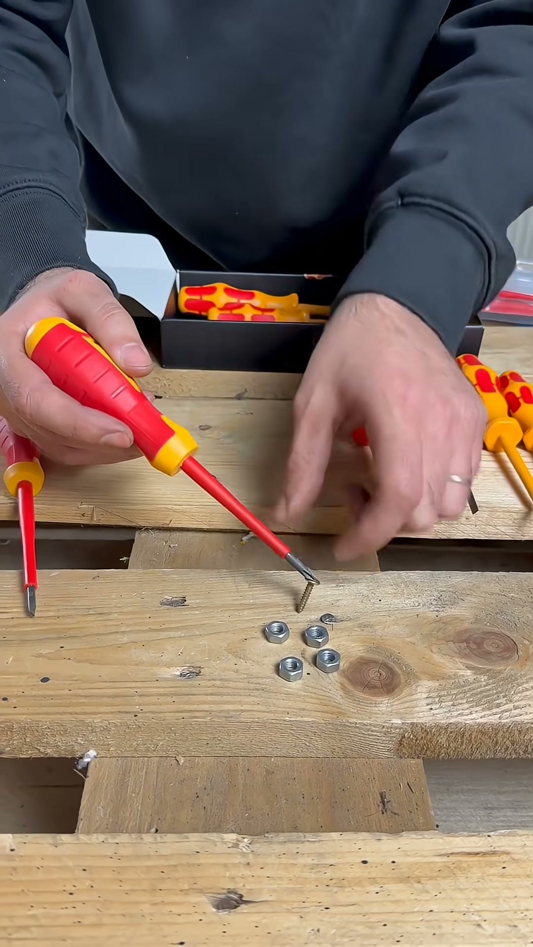 Schraubendreherspitze hält eine Schraube magnetisch an, darunter liegen Muttern auf der Holzwerkbank