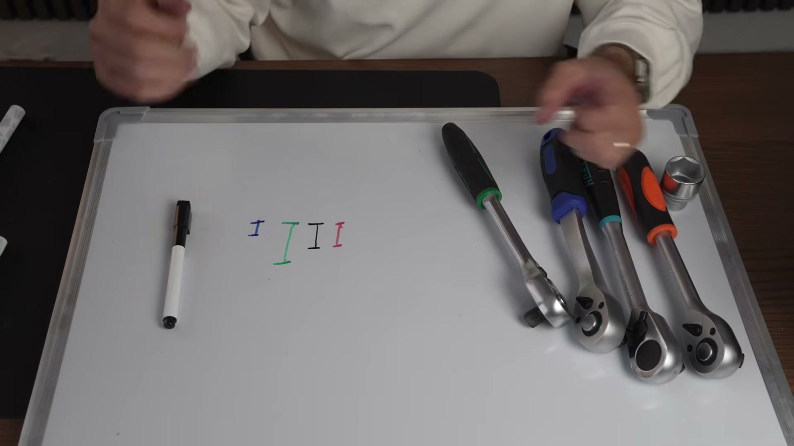 Ein Whiteboard mit vier Markerstrichen, die den Ausholweg pro Klick je Ratsche zeigen.